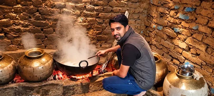 A producer stirring a large pan over a wood fire in a traditional mountain kitchen