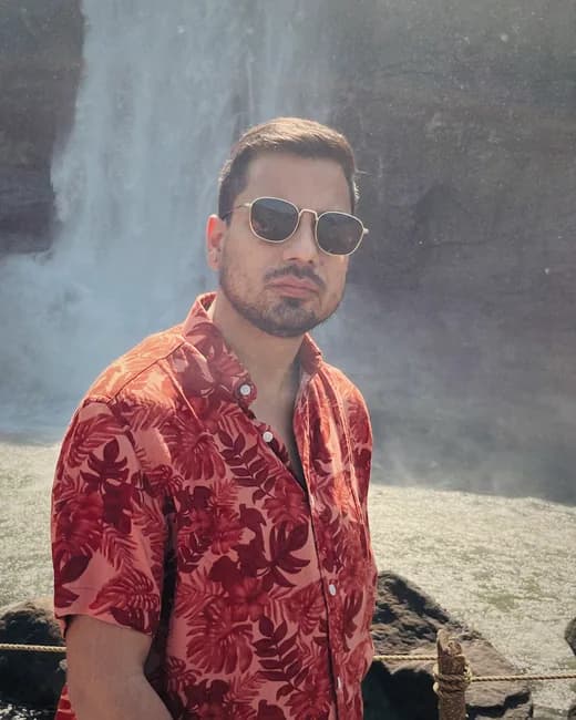 Rahul, co-founder of HimVeda, in a red printed shirt and sunglasses in front of a waterfall