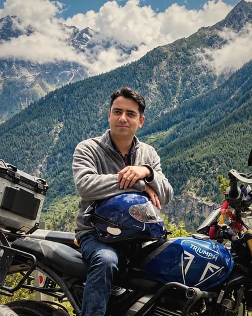 Sudhir Chambail, co-founder of HimVeda, seated on a motorcycle with forested Himalayan peaks behind him